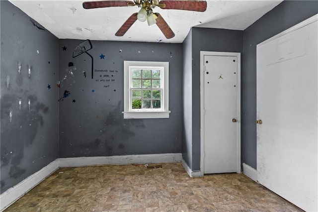 spare room featuring baseboards, ceiling fan, and stone finish floor