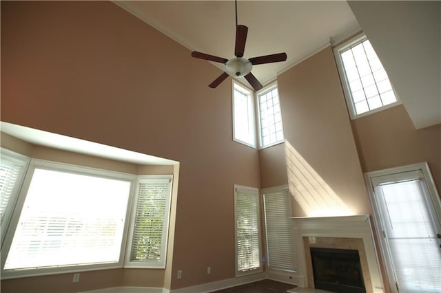 unfurnished living room with ceiling fan, plenty of natural light, a towering ceiling, and a fireplace