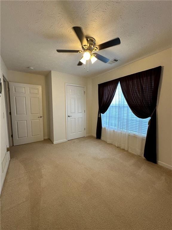 unfurnished bedroom with a textured ceiling, light colored carpet, and ceiling fan