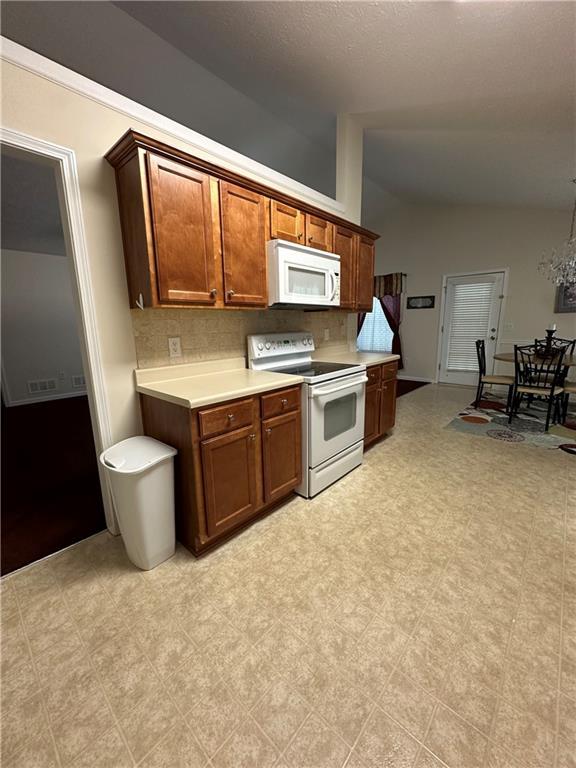 kitchen featuring vaulted ceiling, an inviting chandelier, backsplash, and white appliances