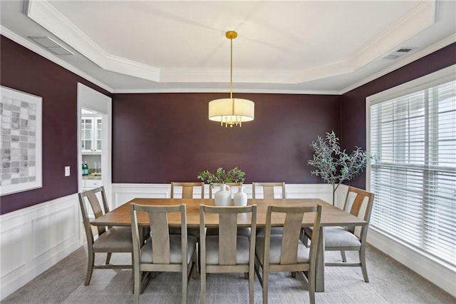 carpeted dining area with a wainscoted wall, visible vents, a tray ceiling, crown molding, and a chandelier