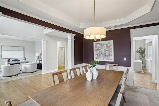 dining area featuring crown molding, a raised ceiling, ornate columns, and wood finished floors