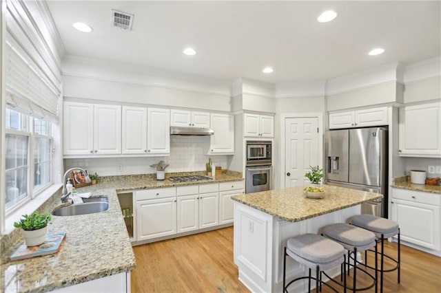 kitchen featuring visible vents, a sink, stainless steel appliances, under cabinet range hood, and a center island