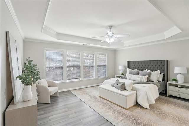 bedroom with a tray ceiling, wood finished floors, crown molding, baseboards, and ceiling fan