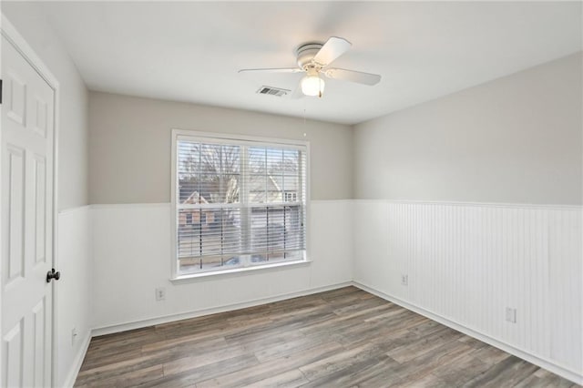 spare room with visible vents, wainscoting, ceiling fan, and wood finished floors