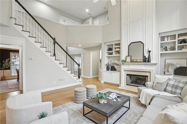 living room with stairs, built in features, baseboards, and light wood-type flooring