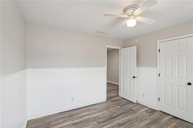 unfurnished bedroom with a wainscoted wall, visible vents, wood finished floors, and a ceiling fan