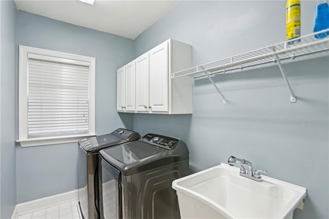 clothes washing area featuring cabinet space, washer and dryer, baseboards, and a sink