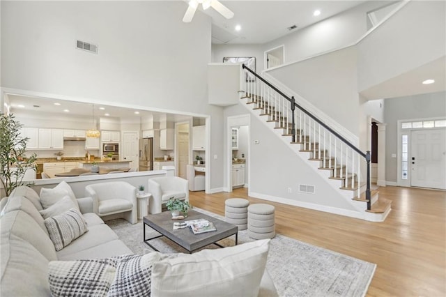 living room with baseboards, visible vents, stairs, a towering ceiling, and light wood-type flooring