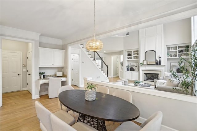 dining room featuring a notable chandelier, a glass covered fireplace, stairway, crown molding, and light wood finished floors