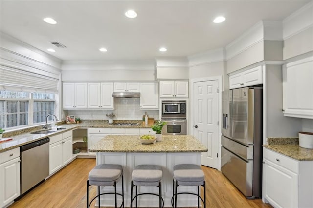 kitchen with a breakfast bar area, a sink, stainless steel appliances, under cabinet range hood, and a center island