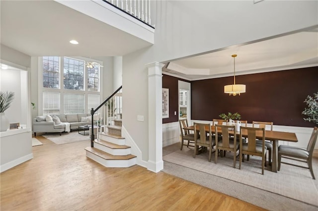 dining area with wood finished floors, recessed lighting, decorative columns, a towering ceiling, and stairs