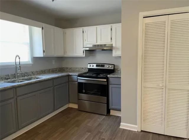 kitchen with gray cabinetry, under cabinet range hood, stainless steel electric stove, dark wood-style floors, and a sink