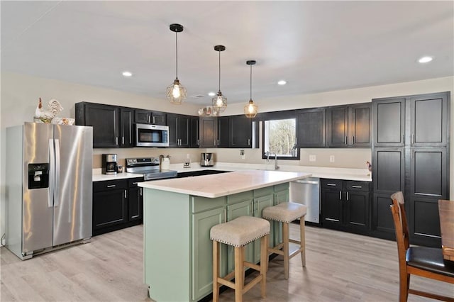 kitchen with a breakfast bar, hanging light fixtures, appliances with stainless steel finishes, a kitchen island, and light hardwood / wood-style floors