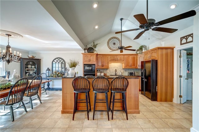 kitchen with a breakfast bar, a center island with sink, decorative backsplash, and black appliances