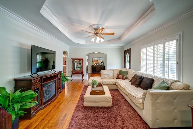 living room featuring wood-type flooring, ornamental molding, ceiling fan, and a tray ceiling