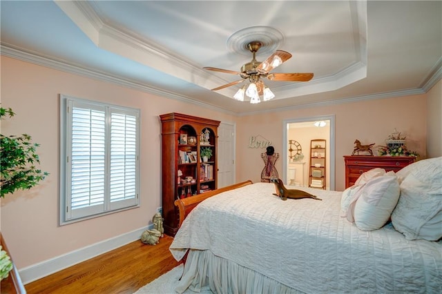 bedroom with crown molding, hardwood / wood-style floors, a tray ceiling, and ceiling fan