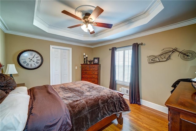 bedroom with crown molding, a tray ceiling, light hardwood / wood-style floors, and ceiling fan