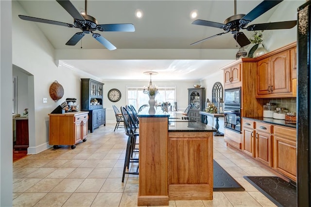 kitchen with a breakfast bar, black oven, built in microwave, a center island, and light tile patterned floors