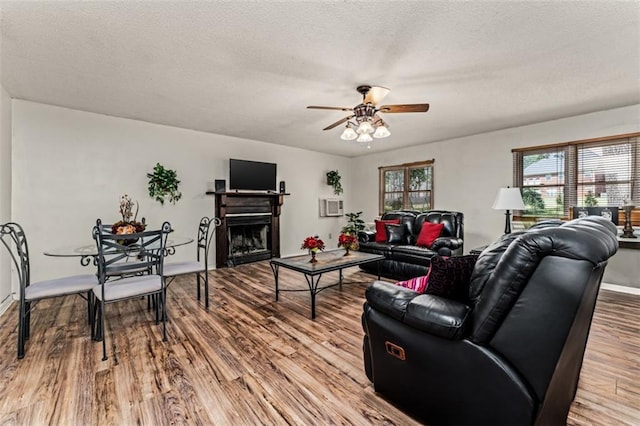 living room featuring a ceiling fan, a textured ceiling, wood finished floors, and a fireplace