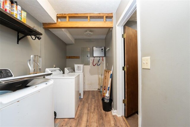 laundry room with light hardwood / wood-style flooring, washing machine and dryer, and electric panel