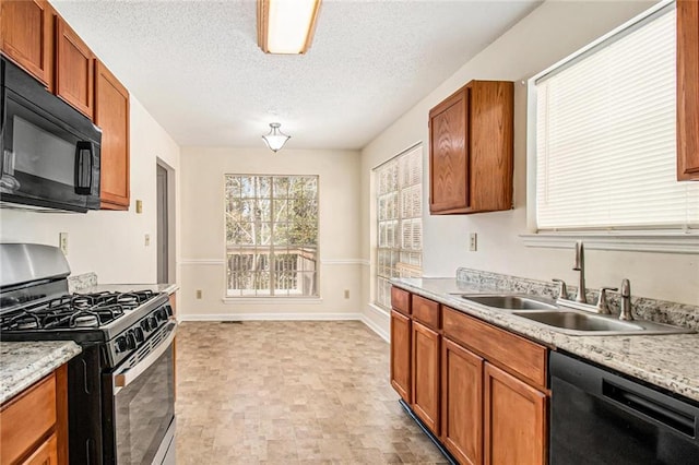 kitchen with brown cabinetry, baseboards, a sink, black appliances, and a textured ceiling