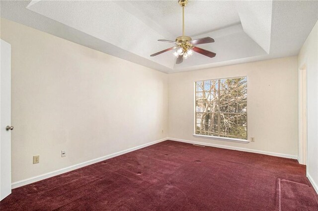 empty room with baseboards, a tray ceiling, ceiling fan, a textured ceiling, and carpet flooring