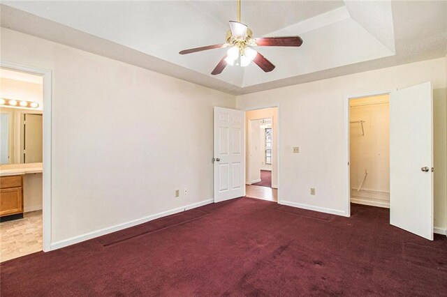 unfurnished bedroom featuring a tray ceiling, baseboards, a walk in closet, and carpet flooring