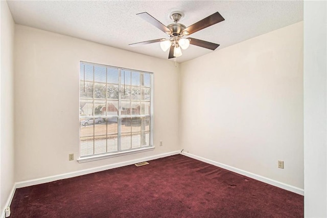 spare room with visible vents, a ceiling fan, a textured ceiling, dark carpet, and baseboards