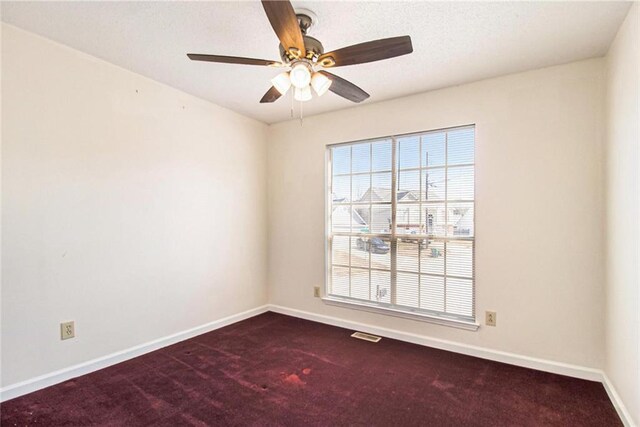 unfurnished room with visible vents, dark carpet, a ceiling fan, and baseboards