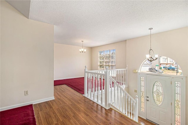 entrance foyer with a textured ceiling, baseboards, an inviting chandelier, and wood finished floors