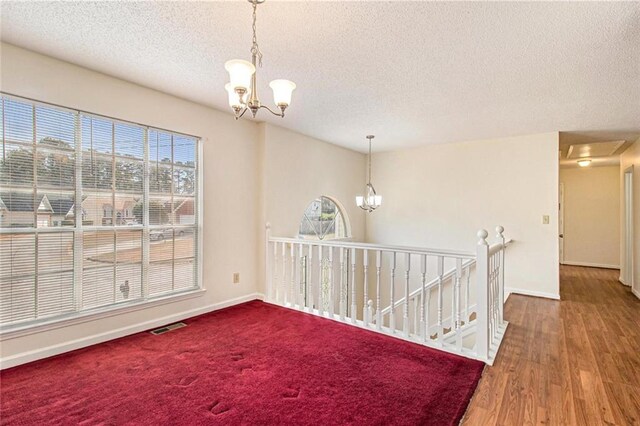 unfurnished room with visible vents, baseboards, a chandelier, wood finished floors, and a textured ceiling