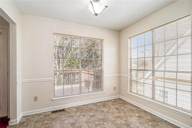 spare room with visible vents, a textured ceiling, and baseboards