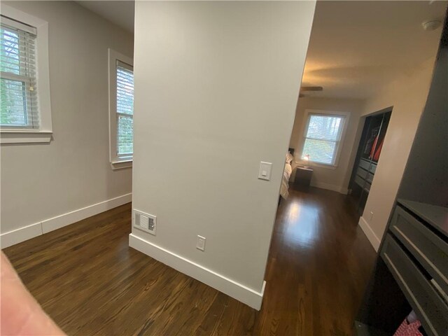 hall with dark wood finished floors, baseboards, and visible vents