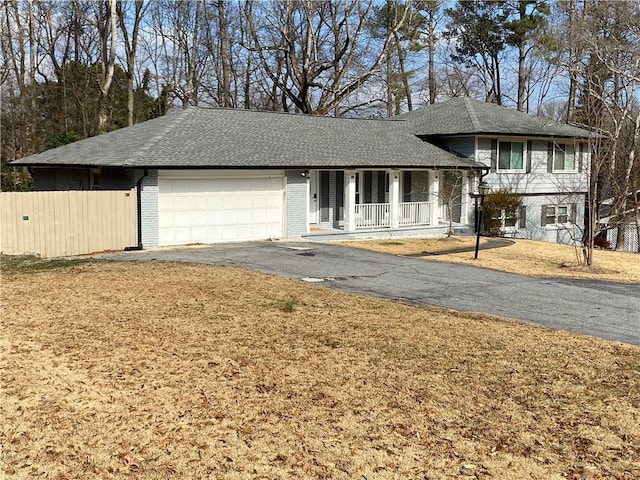 tri-level home featuring driveway, fence, covered porch, a garage, and brick siding
