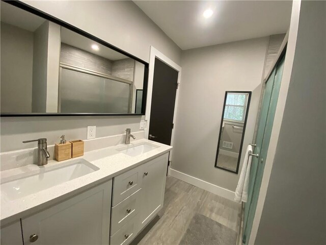 full bath with a sink, double vanity, wood finished floors, and a shower stall