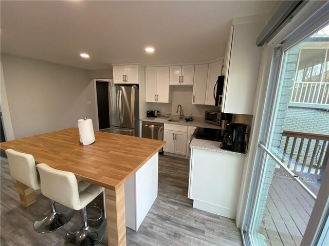kitchen with recessed lighting, wood finished floors, white cabinets, stainless steel appliances, and a sink