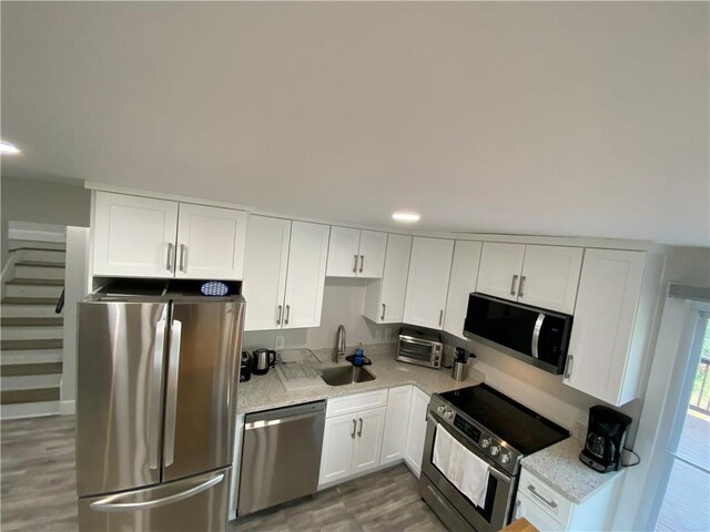 kitchen with light stone countertops, a sink, white cabinets, appliances with stainless steel finishes, and light wood-type flooring