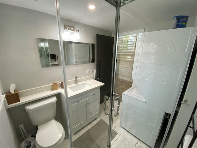 bathroom with toilet, marble finish floor, stacked washer and clothes dryer, a shower with door, and vanity