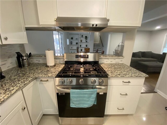 kitchen with ventilation hood, light stone counters, white cabinets, and stainless steel gas range oven