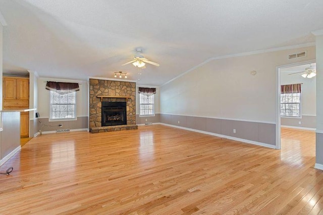 unfurnished living room with vaulted ceiling, a stone fireplace, ceiling fan, light hardwood / wood-style floors, and crown molding