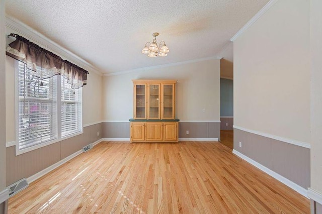 spare room with crown molding, an inviting chandelier, a textured ceiling, and light wood-type flooring