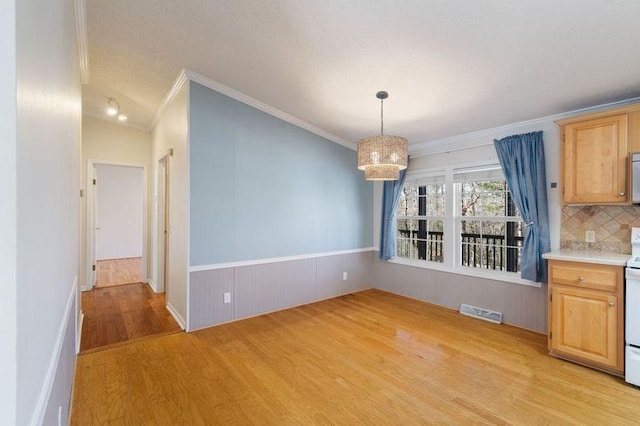 unfurnished dining area featuring an inviting chandelier, ornamental molding, and light wood-type flooring