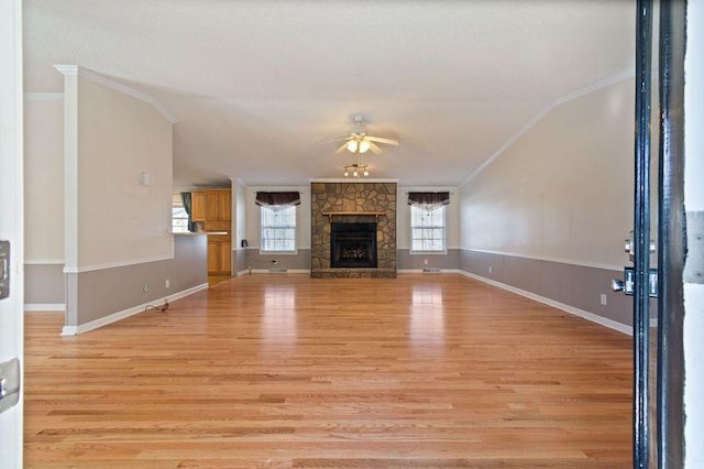 unfurnished living room with ornamental molding, plenty of natural light, a stone fireplace, and light hardwood / wood-style flooring