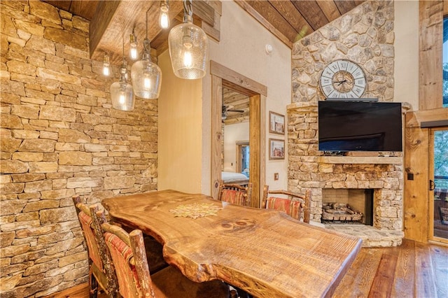 dining room featuring wood ceiling, hardwood / wood-style floors, a stone fireplace, and vaulted ceiling with beams