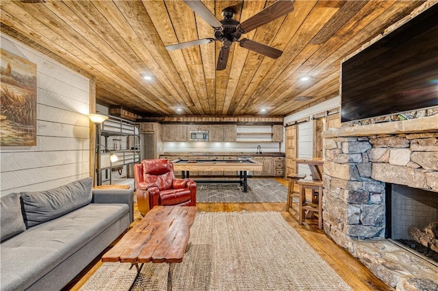 living room featuring light hardwood / wood-style flooring, ceiling fan, wooden walls, and a fireplace