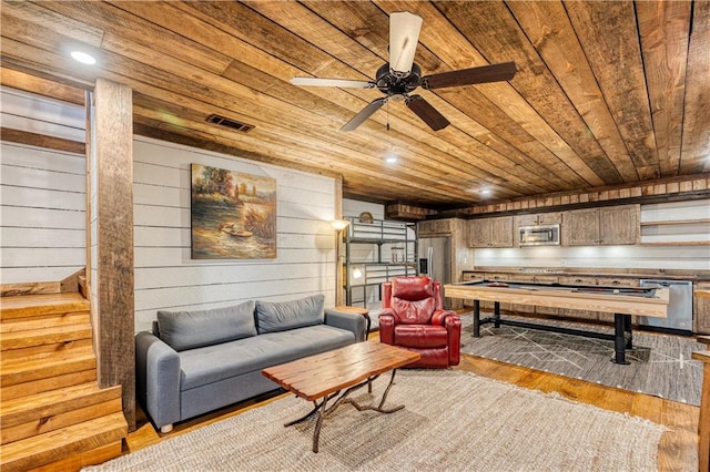 living room with light hardwood / wood-style flooring, ceiling fan, wooden walls, and wooden ceiling