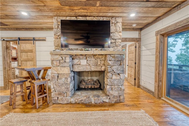 living room with wooden ceiling, a fireplace, hardwood / wood-style flooring, a barn door, and wooden walls