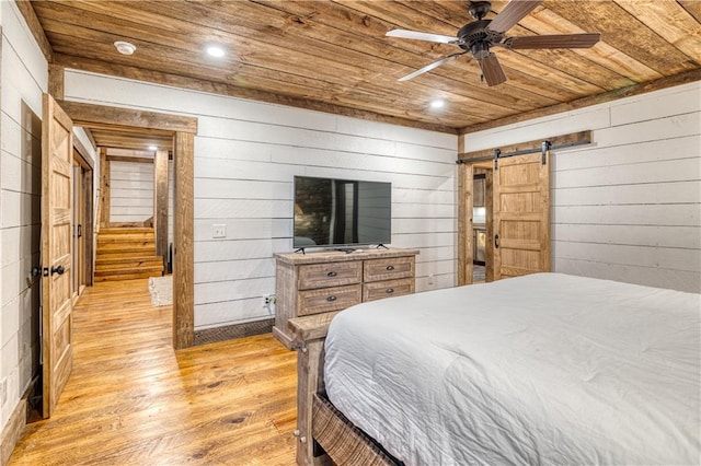 bedroom with wood walls, light hardwood / wood-style flooring, wood ceiling, a barn door, and ceiling fan