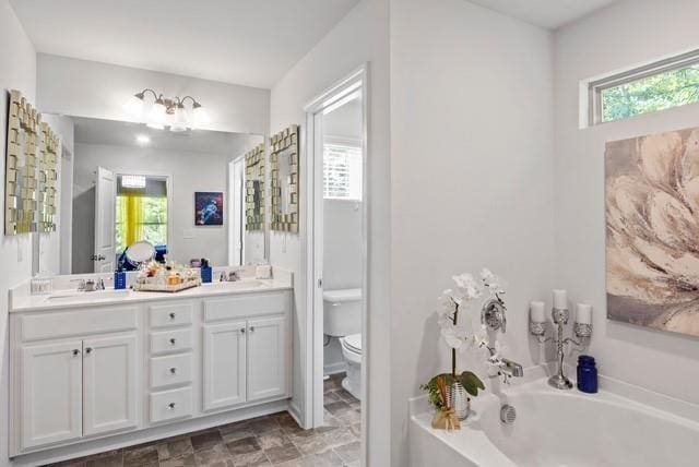 bathroom with a washtub, vanity, and toilet